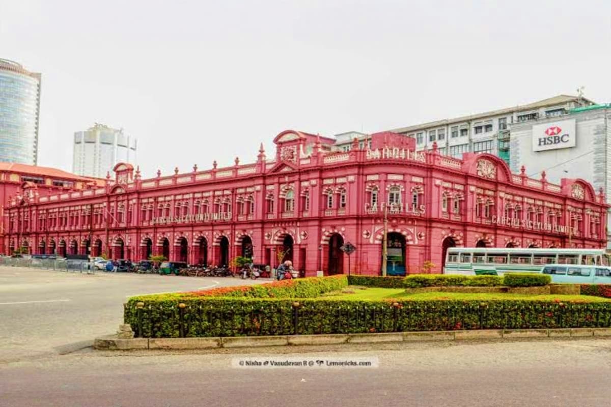 Red colonial building in Kolkata with ornate architecture, manicured hedges, and modern buildings visible in background