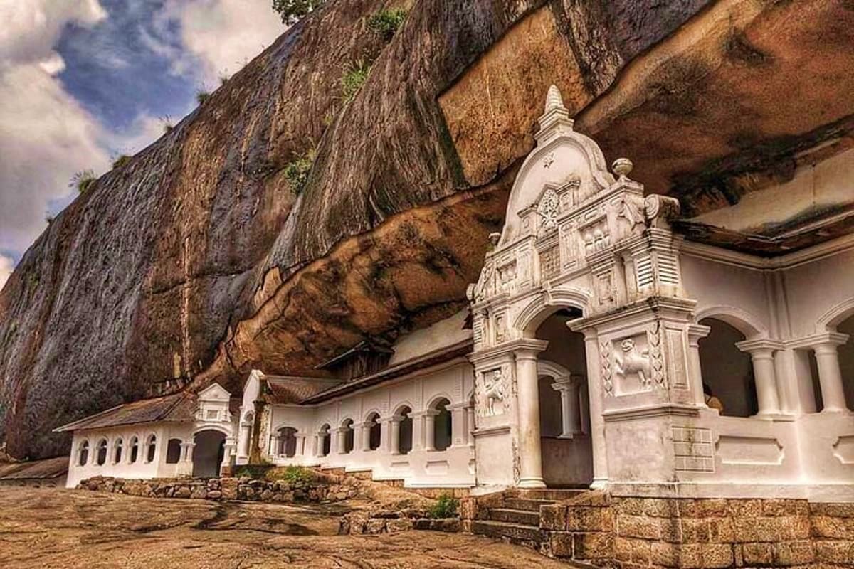 White chapel with ornate bell tower built against massive cliff face with thatched roof overhang