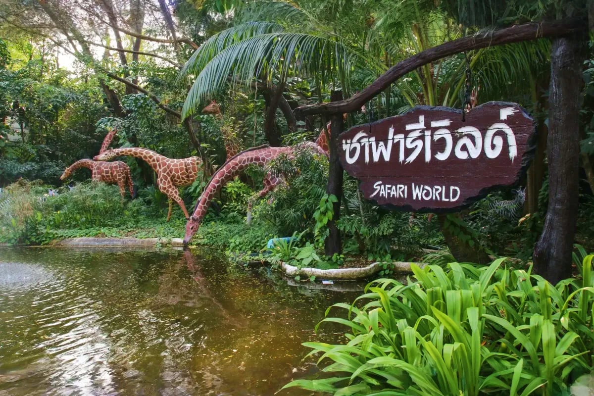 Safari World entrance sign with giraffe sculptures beside pond and tropical vegetation in Bangkok, Thailand