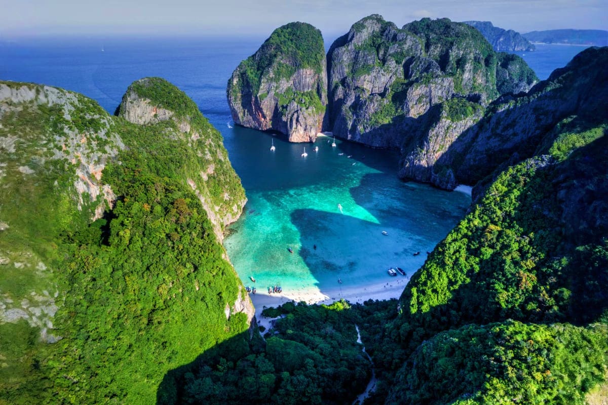 Aerial view of Phi Phi Leh island showing limestone cliffs, turquoise waters, white sand beach, and boats in Maya Bay, Thaila