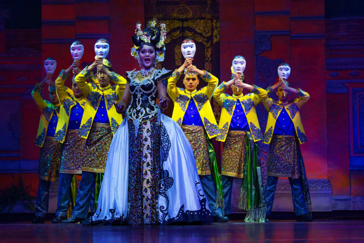 Theatrical performance with performers in elaborate yellow and blue costumes with white face paint and ornate headdresses on 