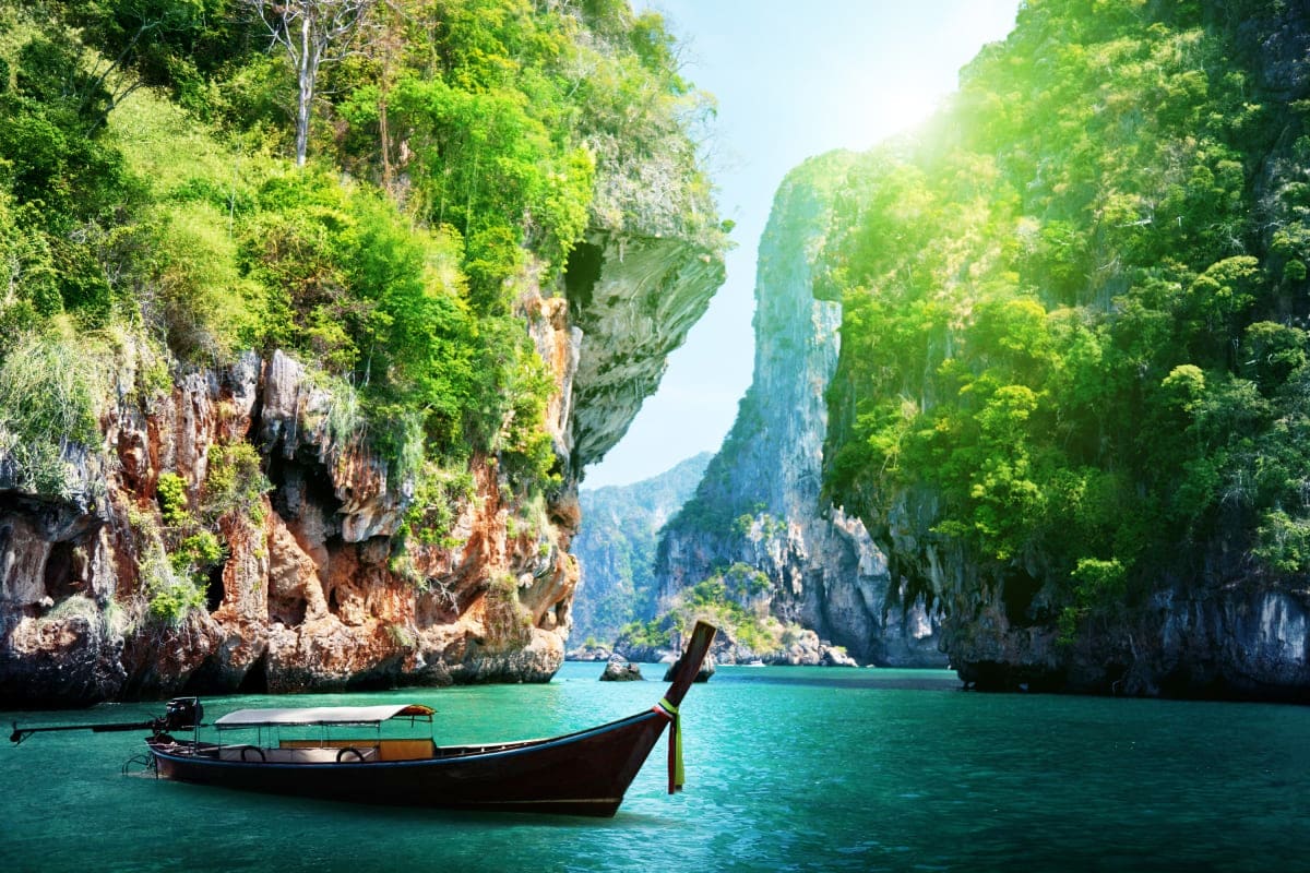 Traditional longtail boat on turquoise water between towering limestone cliffs with lush green vegetation in a tropical bay