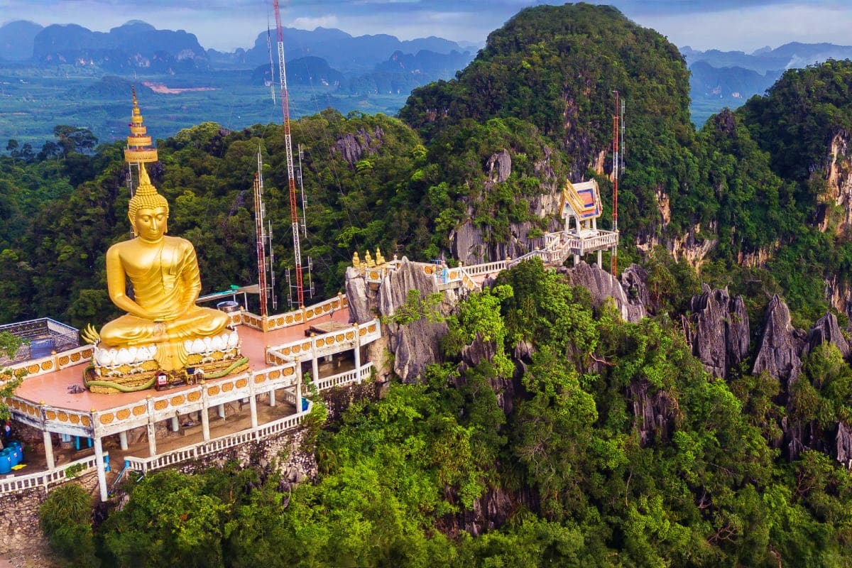 Golden Buddha statue on mountain temple overlooking limestone cliffs and valleys in Phuket, Thailand