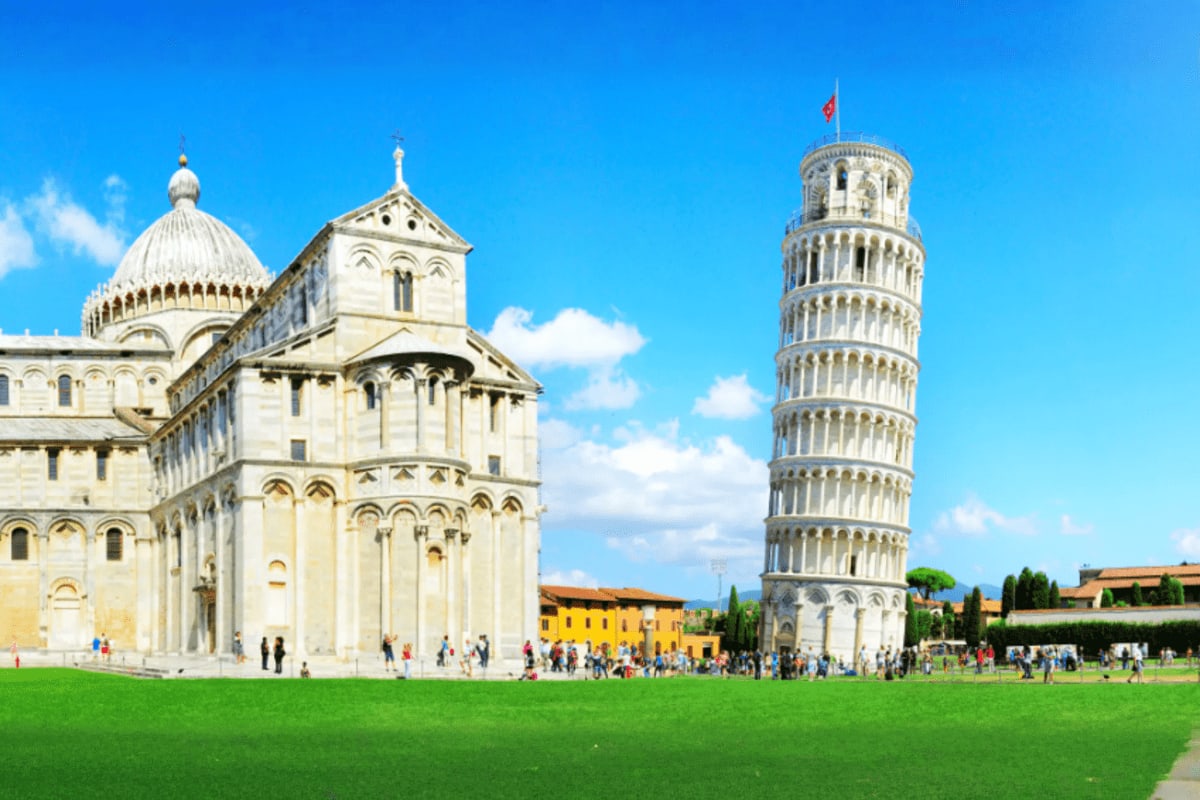 Leaning Tower of Pisa and Cathedral in Pisa's Square of Miracles with tourists on green lawn