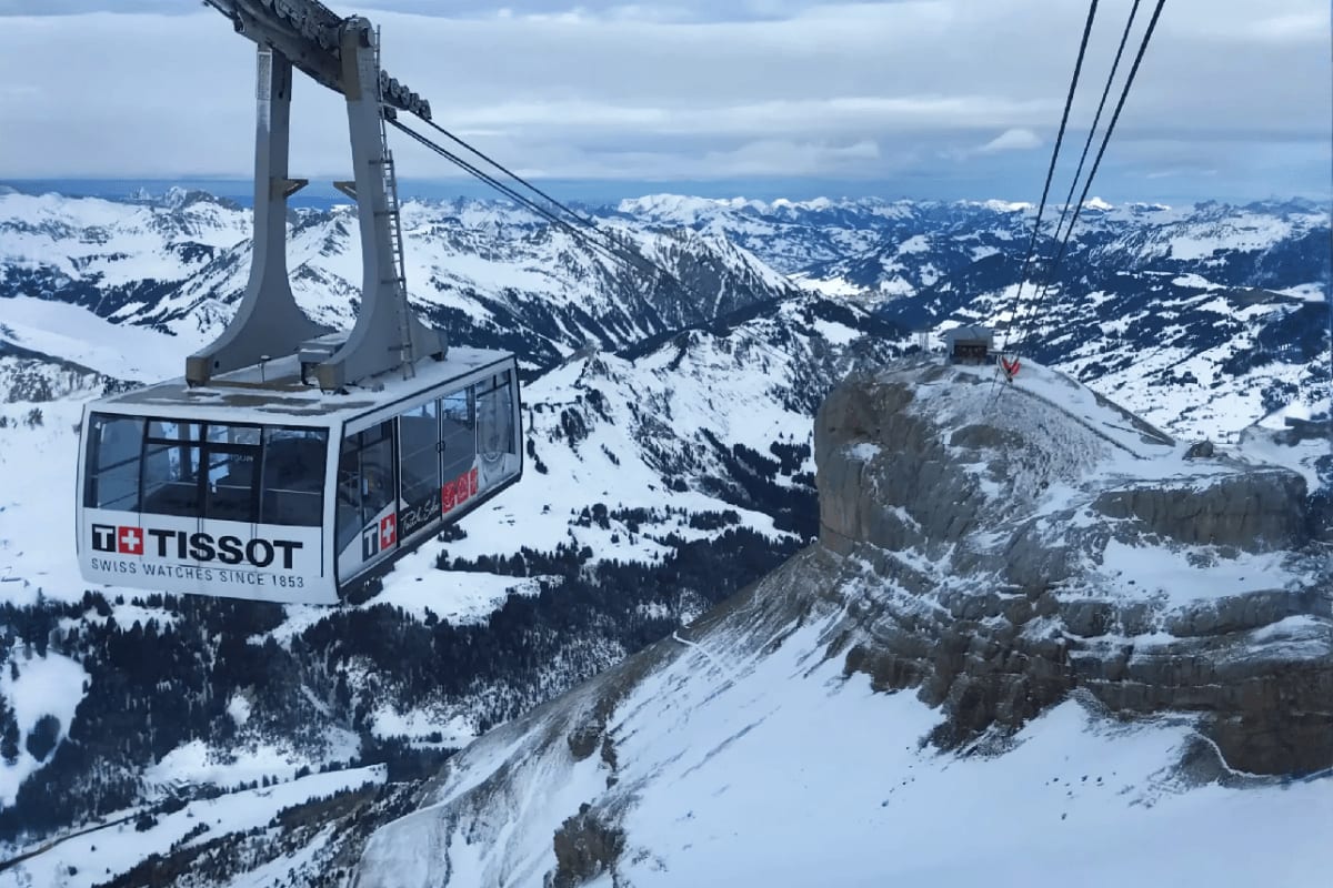 Tissot cable car suspended over snowy Alpine mountains and forested valleys in Switzerland