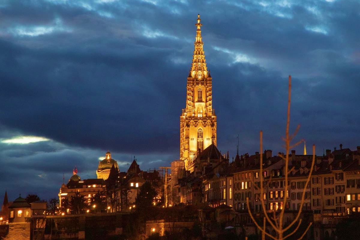 Illuminated Gothic church spire towering over Edinburgh's historic Old Town at dusk with storm clouds overhead