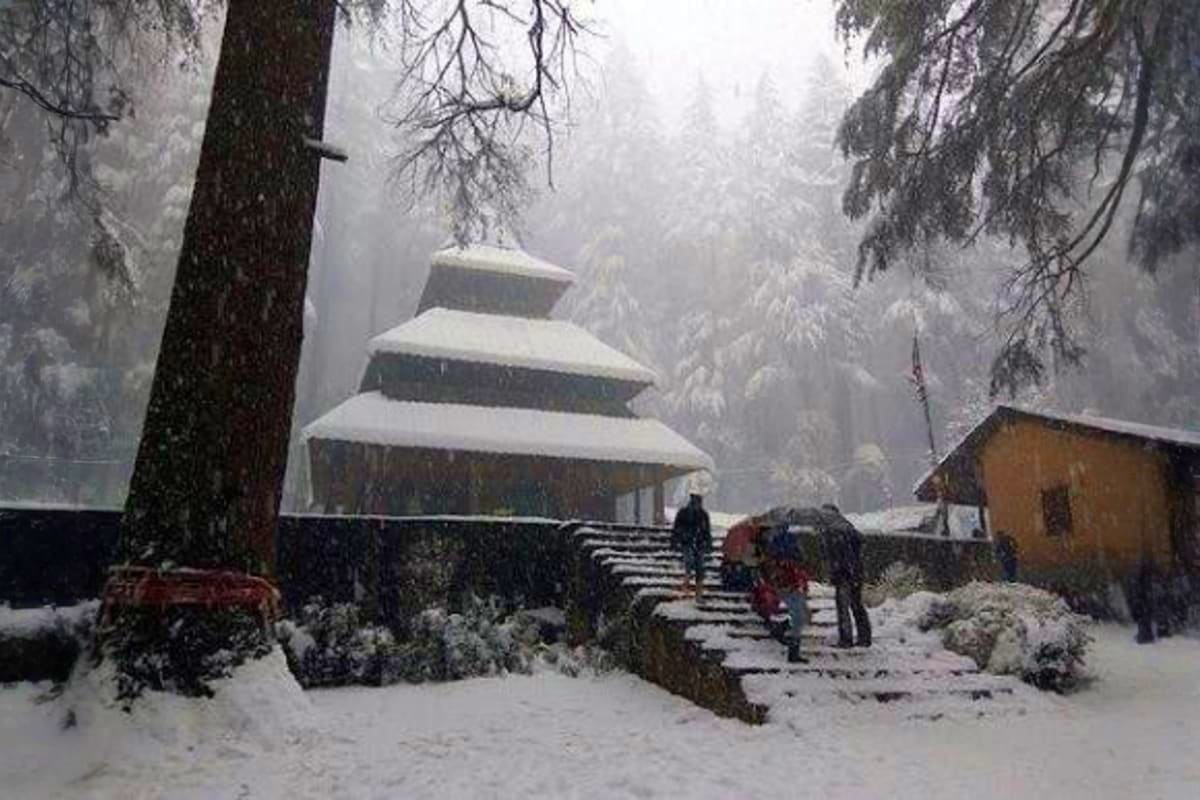 Snow-covered temple with tiered roof surrounded by frost-laden trees and visitors on steps during heavy snowfall in Himachal 