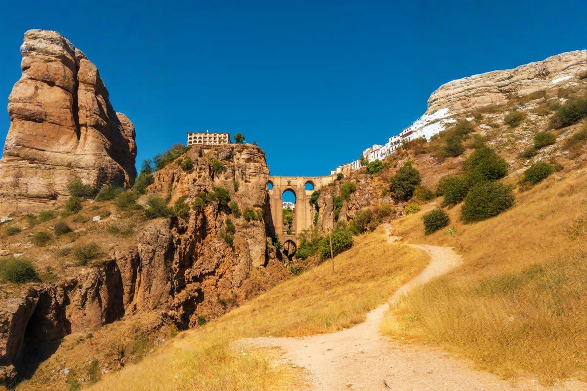 Puente Nuevo bridge spanning a dramatic gorge in Ronda, Spain, with rocky cliffs and whitewashed buildings on hillside under 