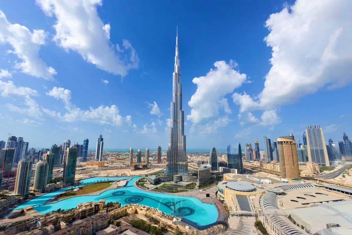 Burj Khalifa towering over Dubai skyline with turquoise water fountain and surrounding skyscrapers on clear blue day