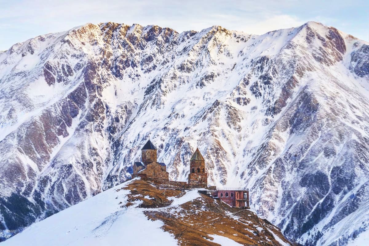Caucasus mountain range with snow-covered peaks and Tsminda Sameba church nestled on a rocky ridge in winter
