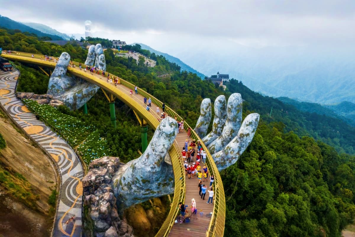 Golden Bridge with giant stone hands nestled in lush green mountains, visitors walking across wooden walkway in Da Nang, Viet