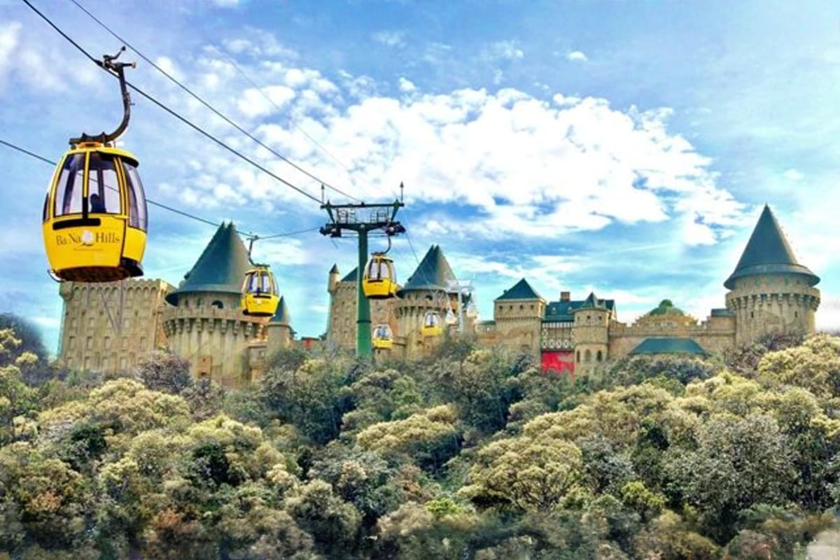 Yellow cable cars suspended above forested hills with medieval castle towers visible in the background under blue sky