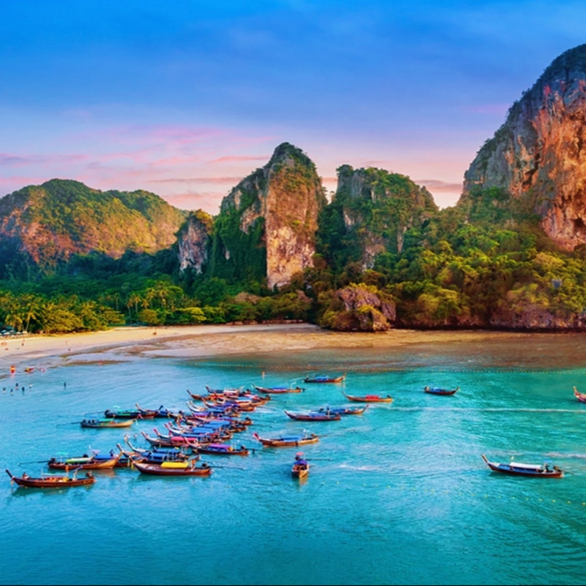 Traditional longtail boats in turquoise waters with limestone cliffs and sandy beach at Railay Beach, Krabi, Thailand