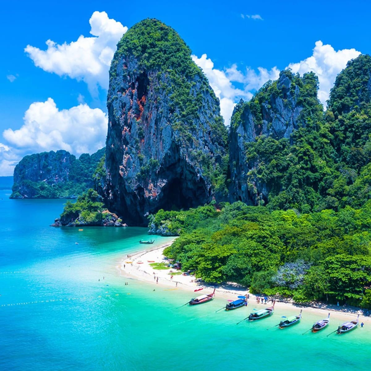 Limestone cliffs and turquoise waters at Railay Beach in Krabi, Thailand, with traditional long-tail boats and white sand bea