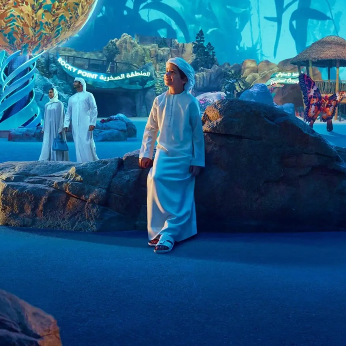 Man in traditional white kandura and blue cap standing at Rocky Point in Abu Dhabi with blue-tinted landscape and other visit