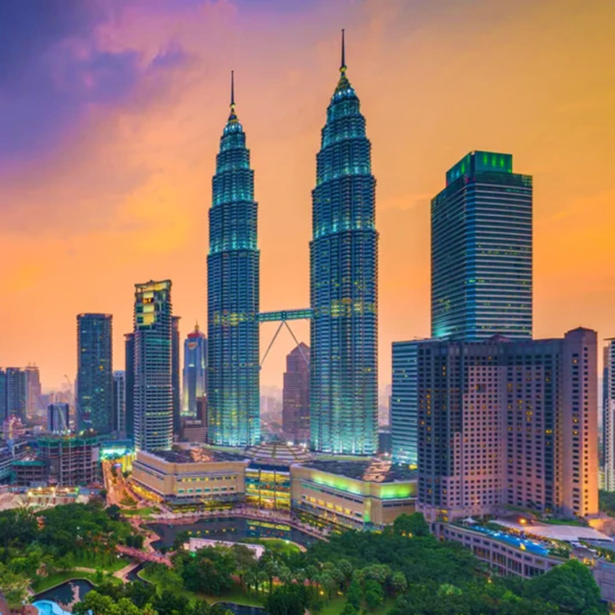 Kuala Lumpur skyline at sunset featuring the illuminated Petronas Twin Towers with surrounding skyscrapers and green parkland