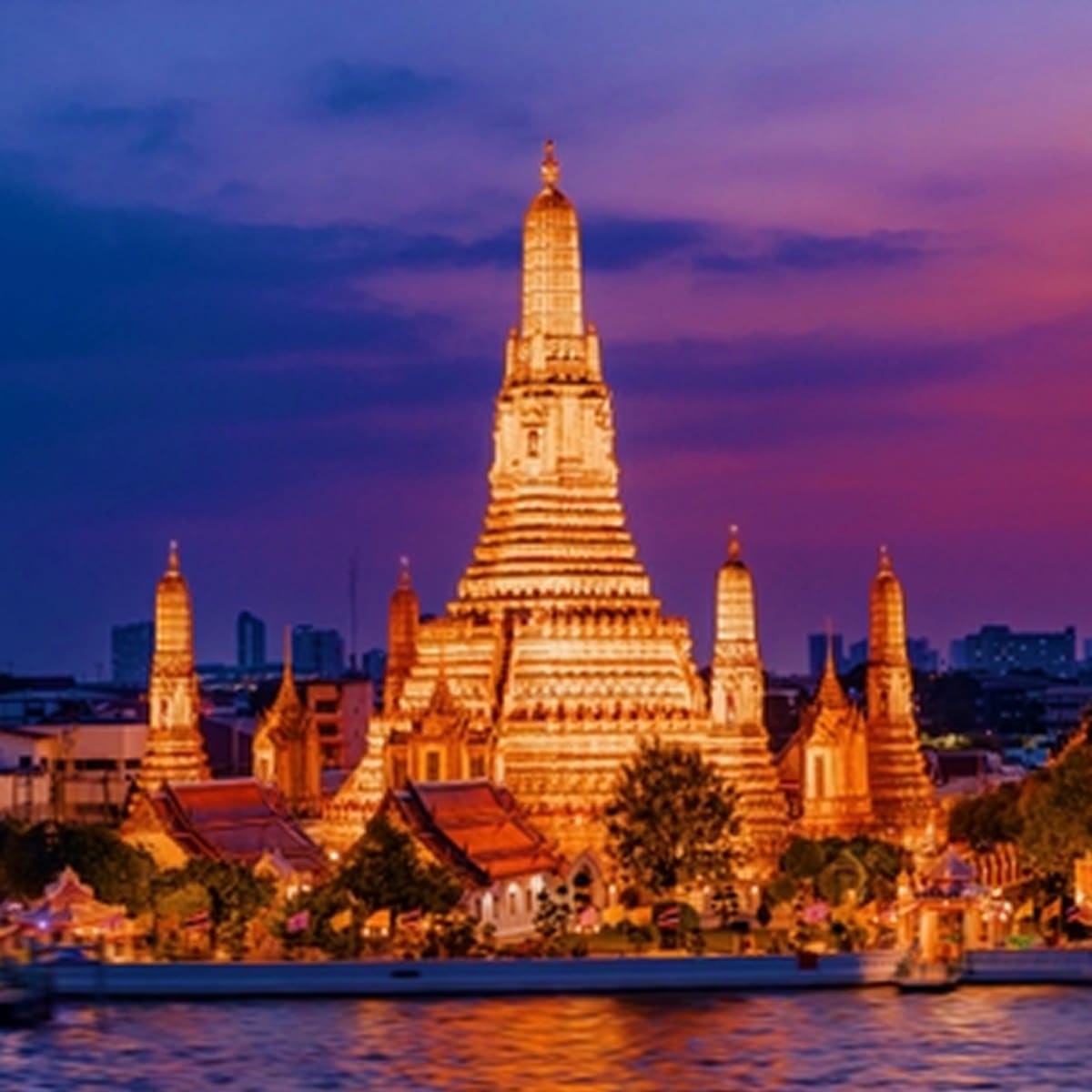 Wat Arun temple illuminated at dusk along the Chao Phraya River in Bangkok, Thailand, with purple twilight sky