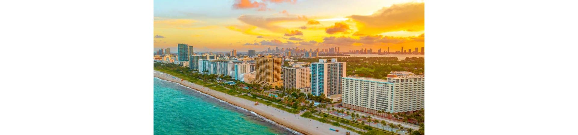 Aerial sunset view of Miami Beach with turquoise ocean, sandy shore, high-rise hotels and residential buildings, and city sky