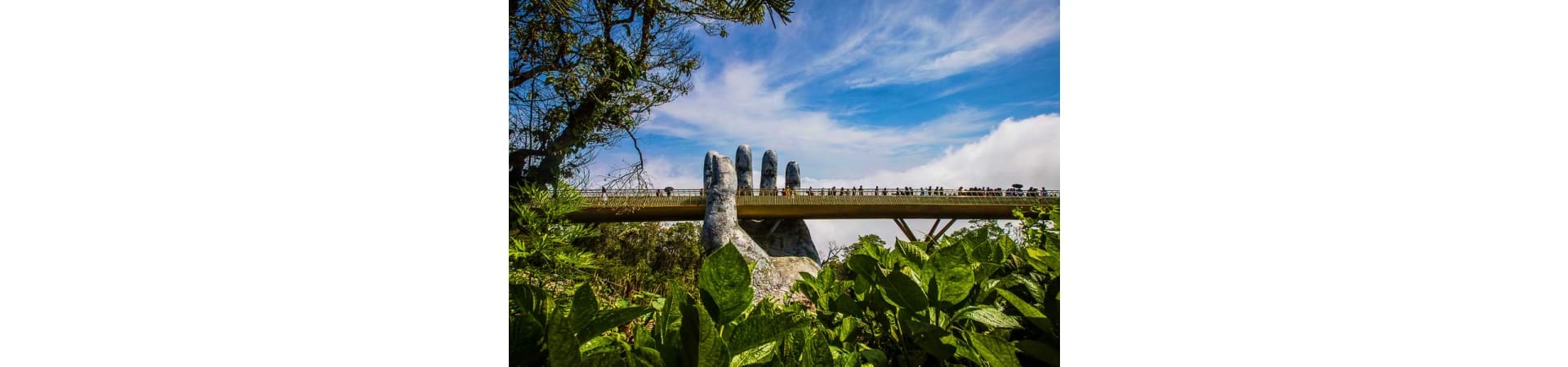 Giant stone hand sculpture emerging from ground beneath wooden bridge with tourists, Da Nang Vietnam