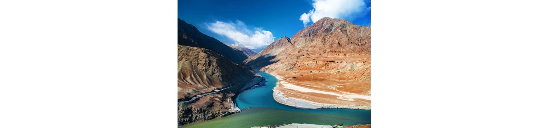 Aerial view of turquoise glacial lake surrounded by barren mountains in Leh, India with snow-capped peaks and clear blue sky