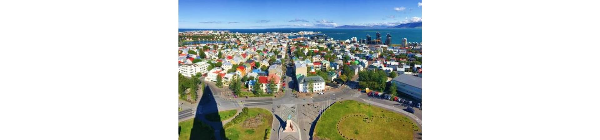Aerial view of Reykjavik cityscape with harbor, residential neighborhoods, and mountains across the bay under clear blue sky