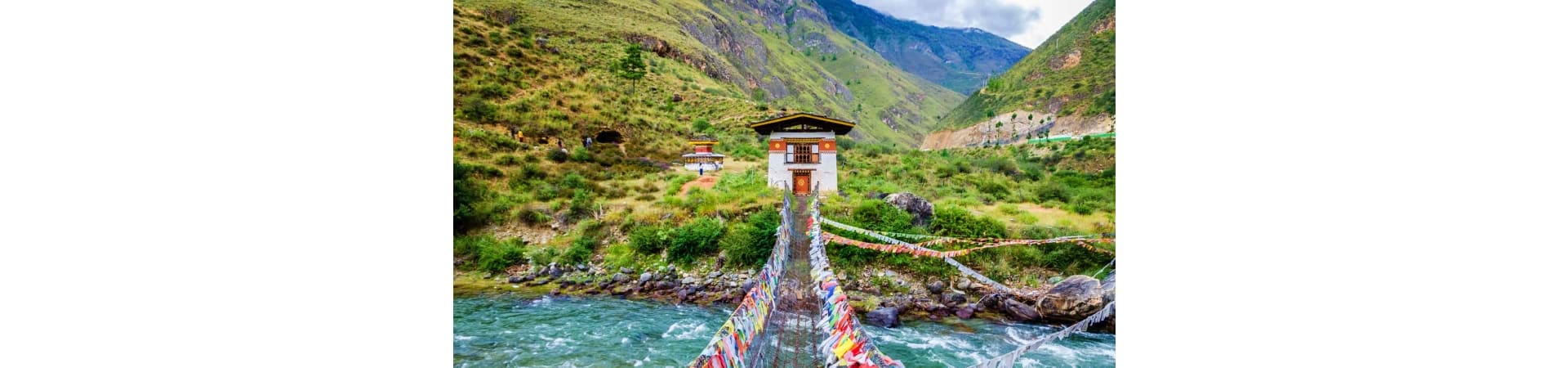 Traditional Bhutanese temple with painted prayer flags spanning across turquoise river in Paro valley mountains