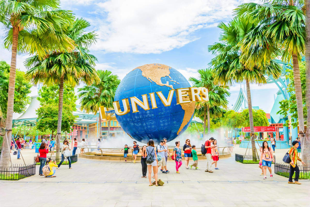 Universal Studios Singapore globe landmark with visitors and palm trees in theme park plaza area