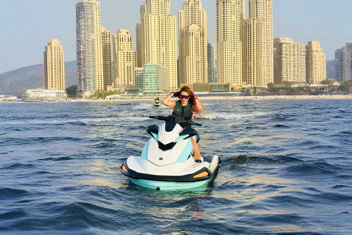 Woman riding jet ski in turquoise water with Dubai Marina high-rise buildings and coastline in background