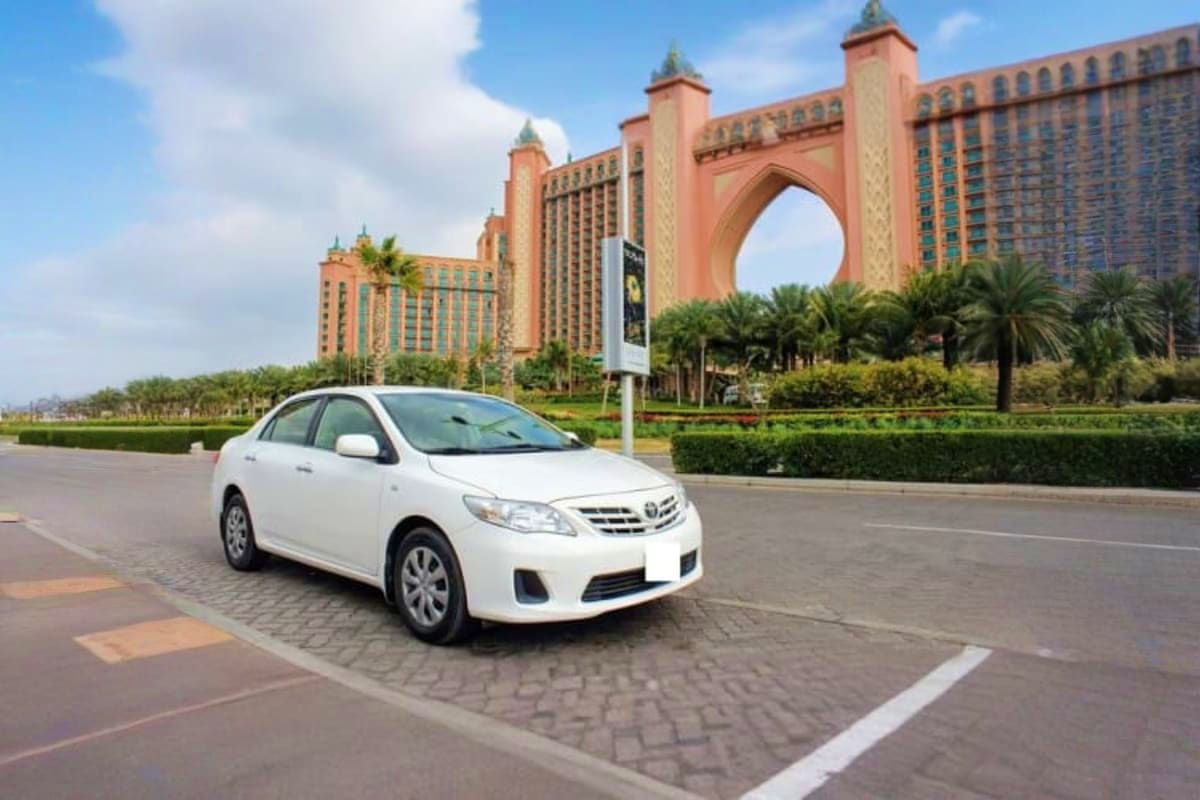 Private Half Day Sightseeing Tour Dubai White Toyota Corolla parked in front of Atlantis The Palm hotel in Dubai with palm trees and blue sky
