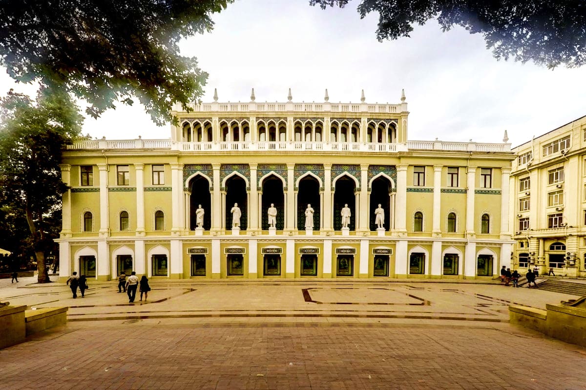 Baku city tour Yellow neoclassical building with white columns and statues in Baku city center plaza with visitors