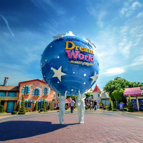 Dream World theme park entrance with large blue globe landmark, colorful buildings, and visitors in the plaza under blue sky