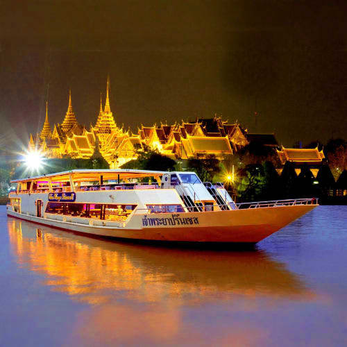 Tourist dinner cruise boat illuminated at night on Chao Phraya River with Golden Palace temple complex glowing in background,
