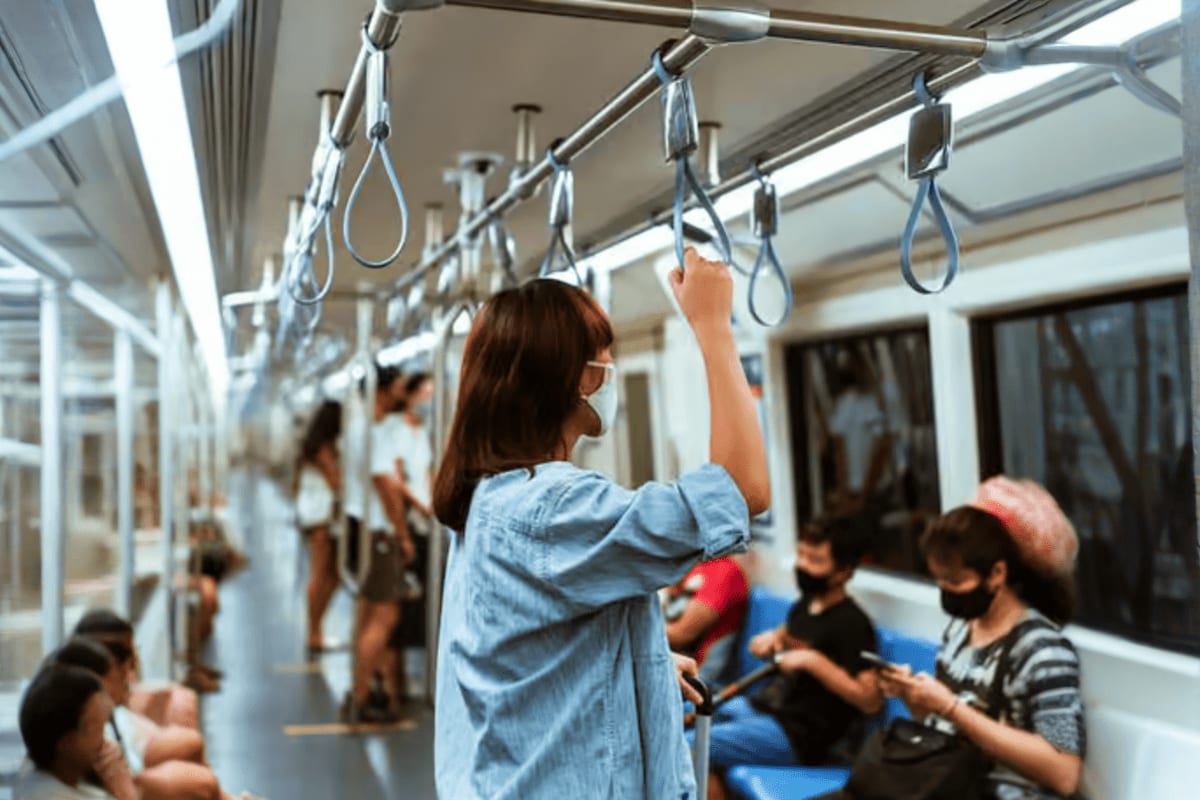 Woman holding handrail inside modern public transport train car with passengers