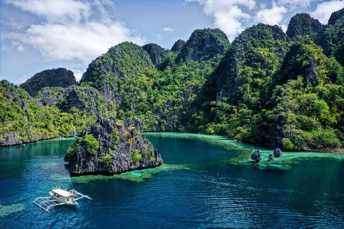 Coron Ultimate Island Day Tour Traditional outrigger boat in turquoise lagoon surrounded by towering limestone cliffs and lush tropical vegetation in Coron,