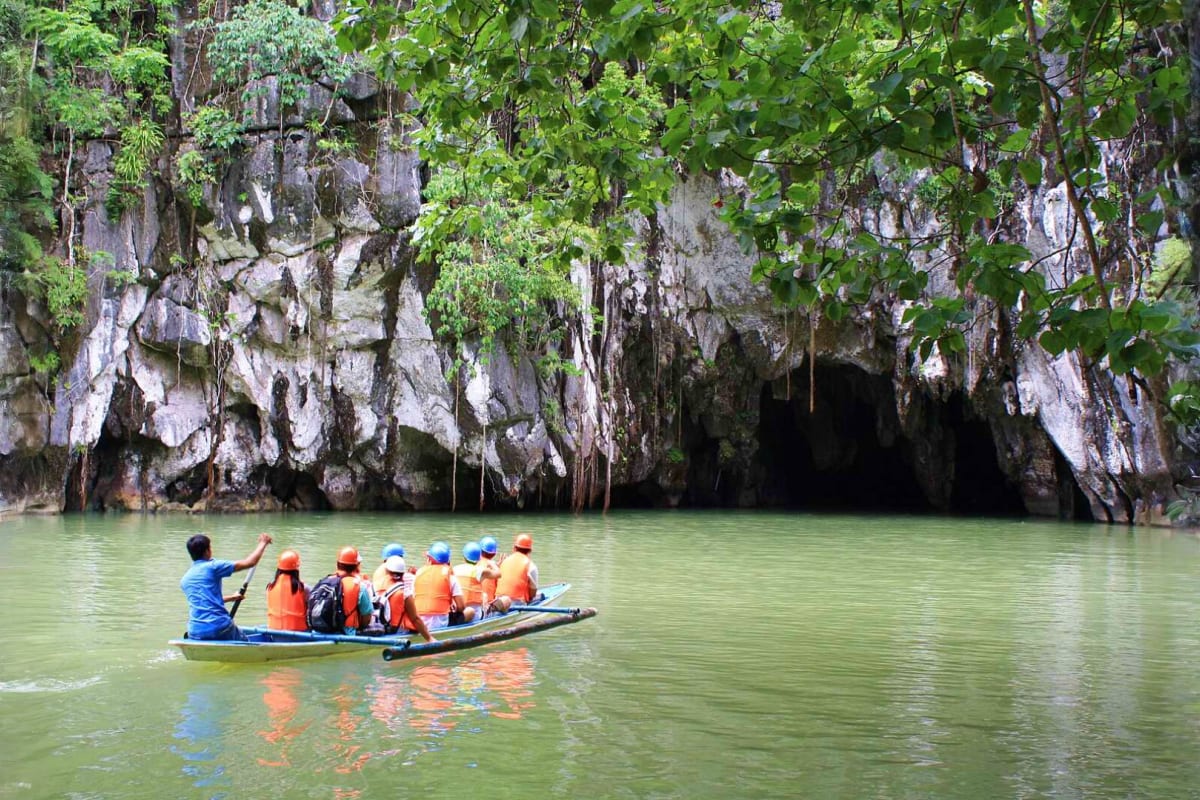 Group of tourists in orange life jackets on small boat approaching cave entrance at Puerto Princesa Underground River, Palawa