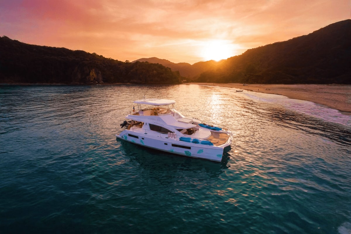 White motor yacht anchored in turquoise waters at sunset with forested limestone cliffs and beach in Phang Nga Bay