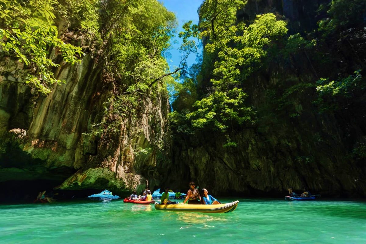 Tourists kayaking in turquoise water beneath towering limestone cliffs in Phang Nga Bay, Thailand