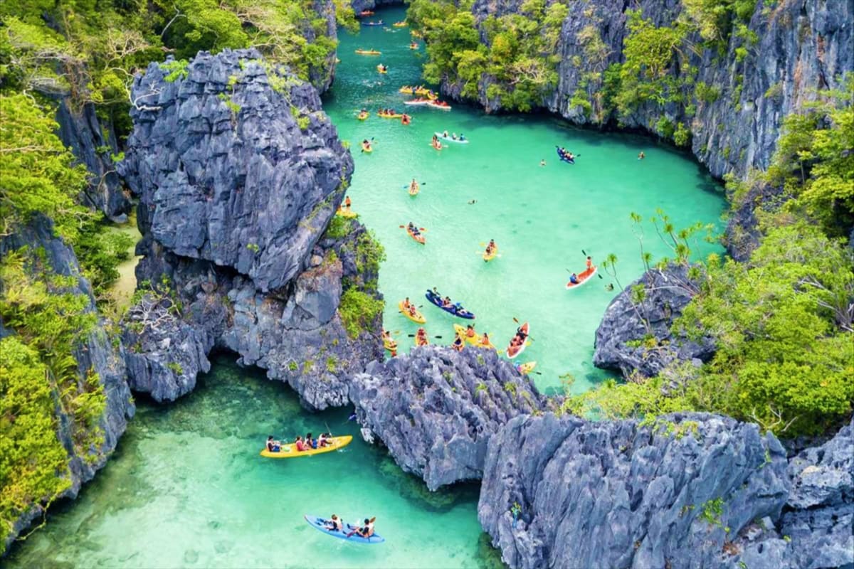 El Nido Island Hopping Tour with Snorkeling Aerial view of turquoise lagoon surrounded by limestone cliffs with tourists kayaking and swimming in the clear water