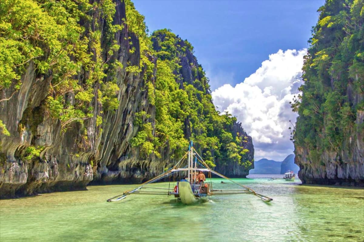 El Nido Island Hopping Tour with Snorkeling Traditional outrigger boat navigating between towering limestone cliffs in clear turquoise waters of El Nido, Philippines