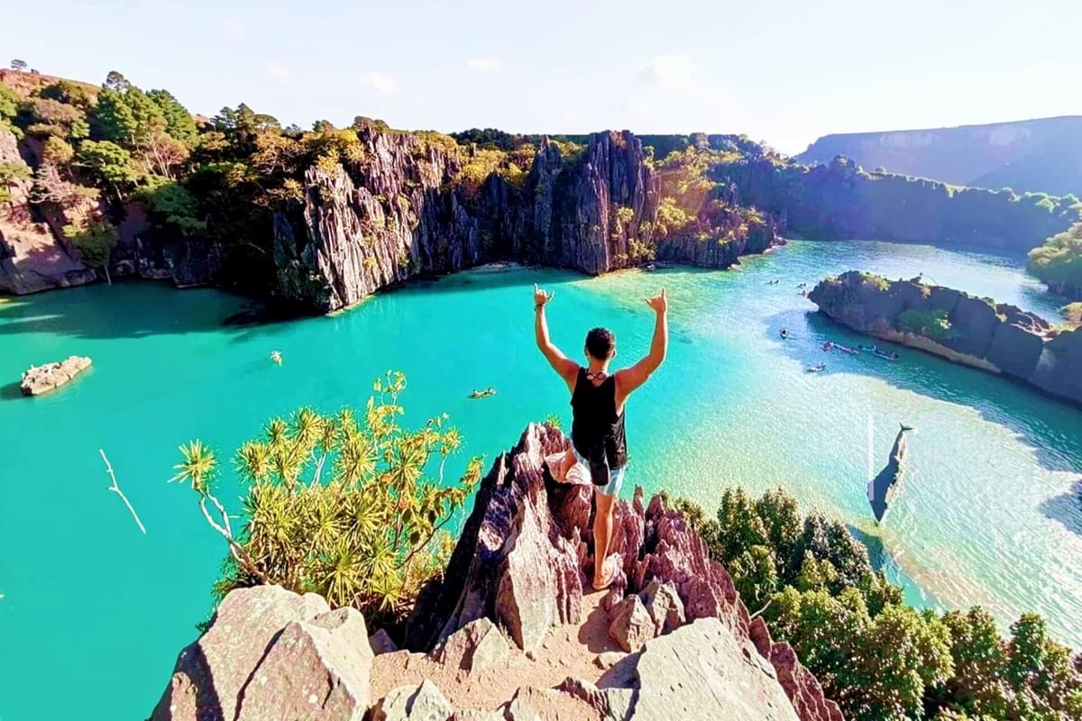 El Nido Tour D Lagoons and Beaches Traveler standing on rocky cliff with arms raised overlooking turquoise lagoon surrounded by tall limestone cliffs in El Nido