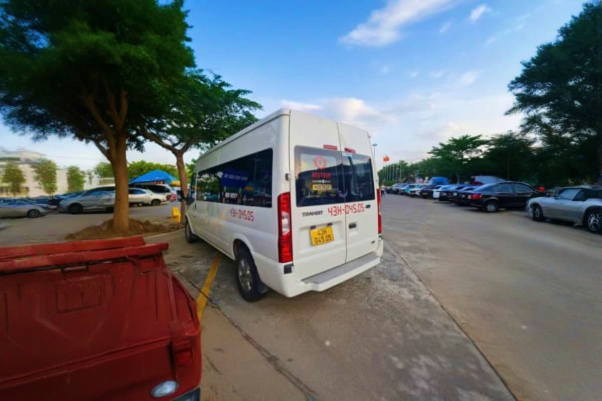 White shuttle van parked in lot with other vehicles and large trees, airport transfer transportation service