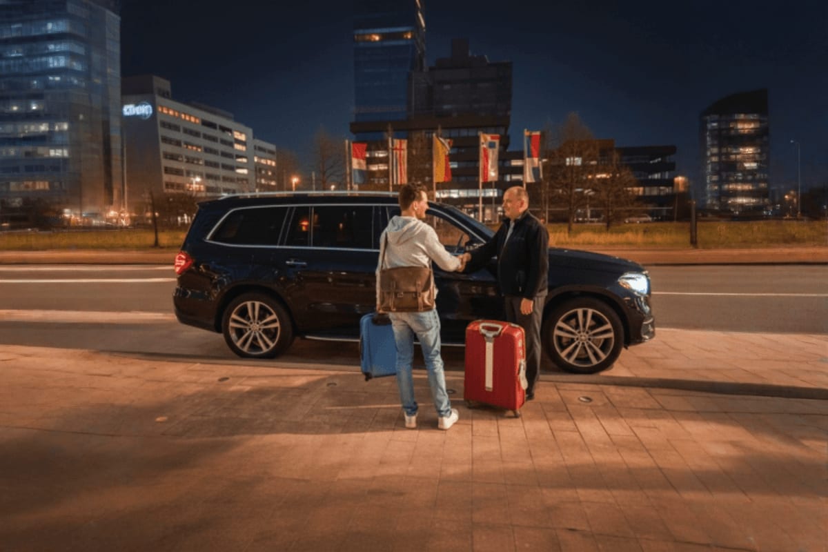 Professional driver greeting passenger with luggage at black SUV during nighttime airport pickup service in urban city area