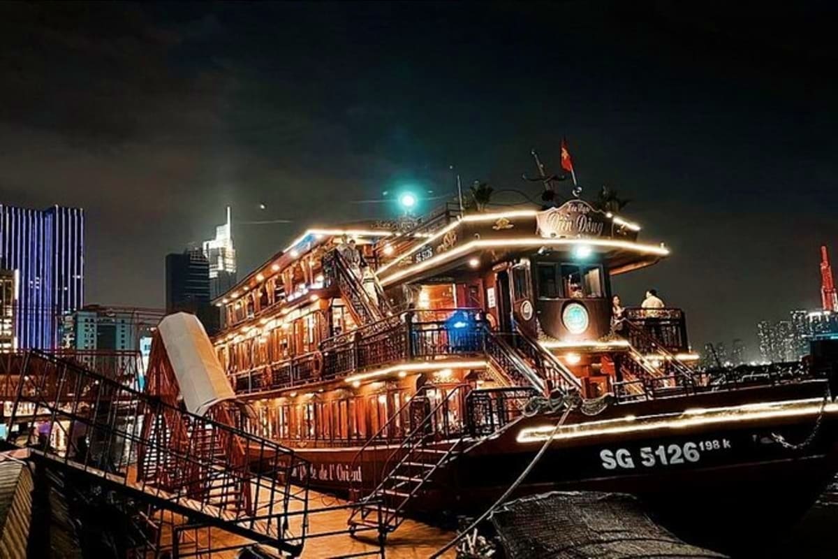 Illuminated wooden junk boat with warm golden lighting docked at night in Singapore harbor with city skyline in background