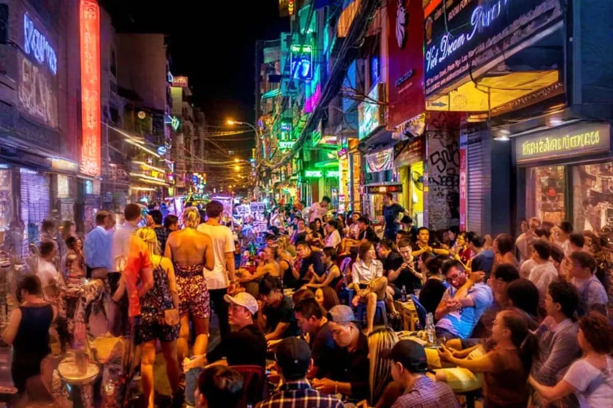 Saigon Street Food Tour By Motobike Crowded night street scene in Ho Chi Minh City with neon signs, street vendors, and tourists gathered for street food dining