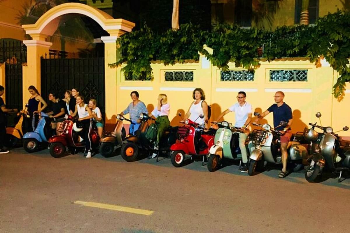 Saigon Street Food Tour By Motobike Group of tourists posing with colorful vintage Vespa scooters in front of yellow colonial building in Vietnam