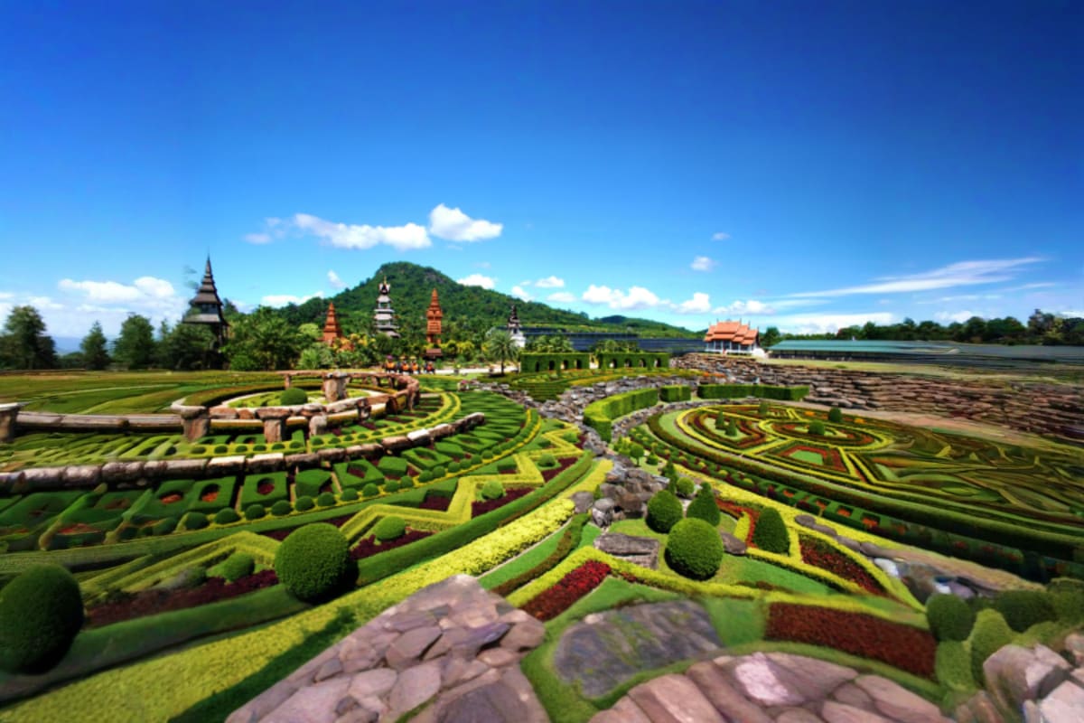 Nong Nooch Tropical Garden Shared Tour Aerial view of Nong Nooch Tropical Garden with ornate topiary designs, temples, and manicured hedges against mountain backdro