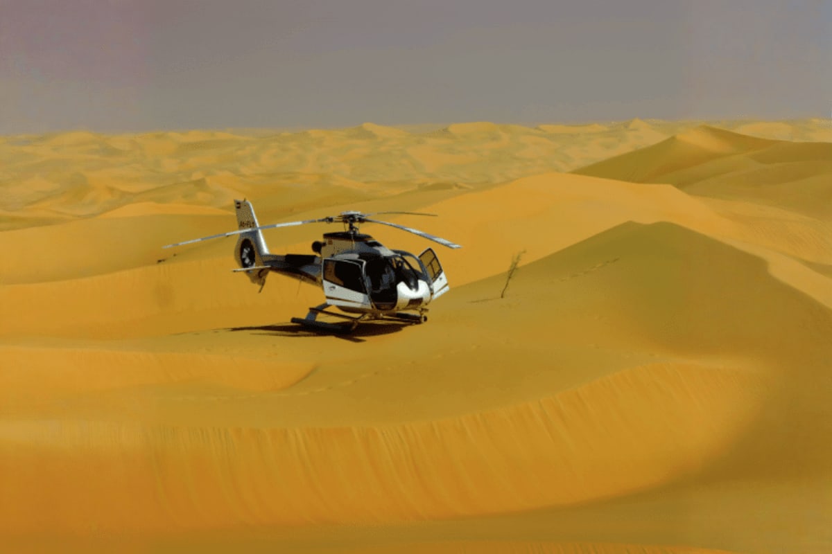 Black and white helicopter landed on golden sand dunes in Dubai desert landscape