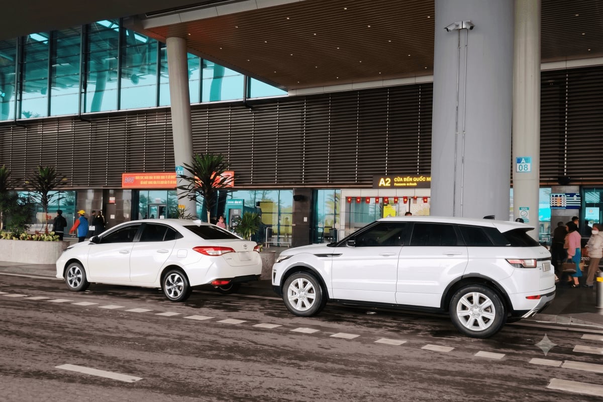 Hanoi Intracity Transfers Two white cars parked outside modern airport terminal building with glass windows and dark horizontal louvers in Hanoi