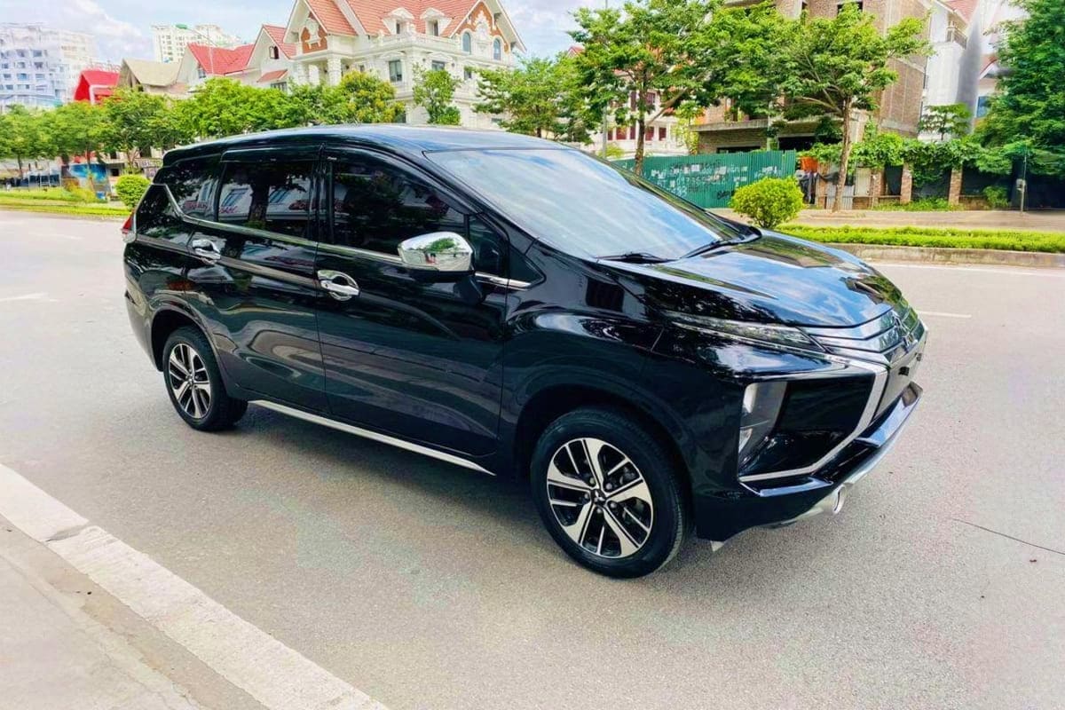 Hanoi Intracity Transfers Black Mitsubishi Xpander minivan parked on city street with colonial villas and green trees in background, Hanoi