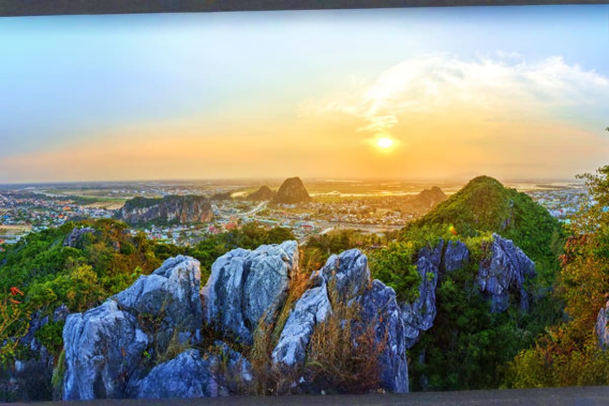 Aerial sunset view of Marble Mountains with limestone peaks, lush green forest, and coastal town sprawling below in Vietnam